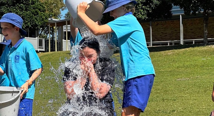 Astudents is pouring a bucket of water over the head of a teacher during a fundraiser event