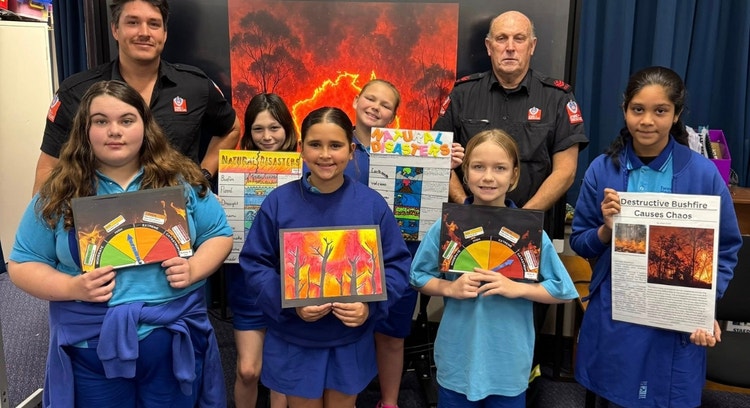 A group of students posing with local firefighters. They are displaying the posters they have made about natural disasters